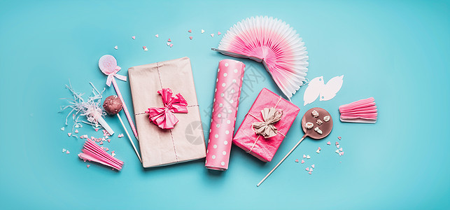 粉红色假日派配件礼品盒与丝带,包装纸,巧克力棒棒糖,派风扇装饰粉彩蓝色背景,顶部视图,平躺,横幅图片