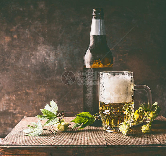 杯啤酒与泡沫冷瓶啤酒与露水啤酒花藤蔓桌子的黑暗墙壁背景,正视图图片