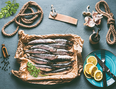 厨房桌子背景上的生沙丁鱼配料柠檬,大蒜草药,用于美味的海鲜烹饪鱼类的烹饪准备图片