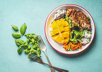 美味的夏季沙拉,烤鸡胸肉芒果碗中,餐具浅蓝色背景下,顶部视图健康低碳水化合物午餐背景图片