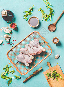 生鸡鸡腿的烹饪准备生鸡腿烤架钢栅栏与配料,草药,香料,酱汁烹饪勺子浅蓝色厨房桌子背景,顶部视图图片