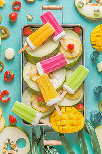 托盘与彩色冰淇淋冰棒与新鲜切片水果浆果成分浅蓝色背景,顶部视图,平躺冷冻热带果汁自制冰淇淋派图片