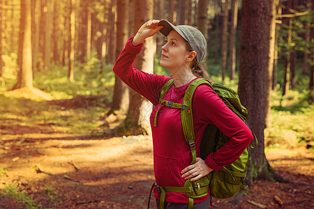 轻的女游客穿着红色的衣服,带着绿色的背包森林里向边看图片