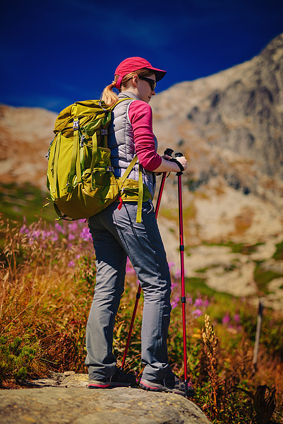 轻的女游客,绿色的背包太阳镜站高山背景上图片