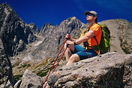 轻人游客,带着绿色的背包电线杆,坐高山上,向边看图片