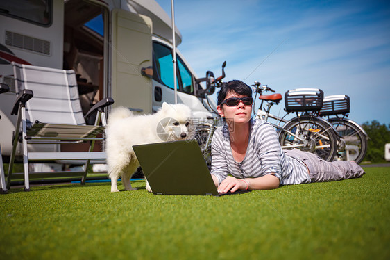 草地上的女人带着只狗看着笔记本电脑房车度假家庭度假旅行,汽车之家度假旅行图片