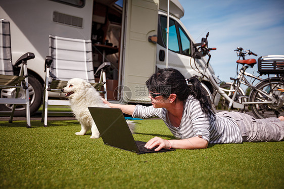 草地上的女人带着只狗看着笔记本电脑房车度假家庭度假旅行,汽车之家度假旅行图片
