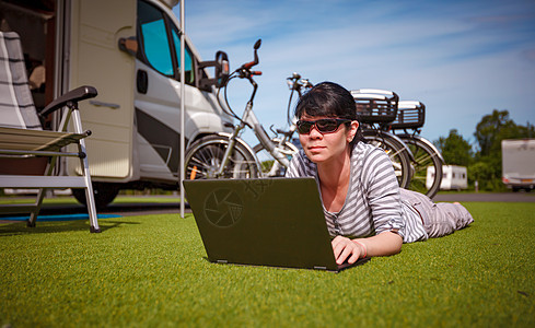 草地上的女人,看着野营附近的笔记本电脑房车度假家庭度假旅行,汽车之家度假旅行图片