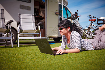 草地上的女人,看着野营附近的笔记本电脑房车度假家庭度假旅行,汽车之家度假旅行图片