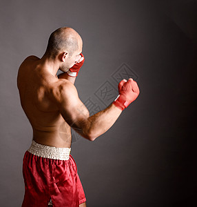 强壮的拳击手武术战士灰色背景上用火热的手击球图片