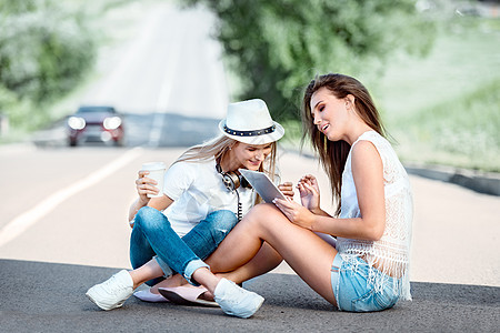 快乐的轻女坐路上,外卖咖啡杯里喝咖啡,戴着音乐耳机,用平板电脑,道路背景下线购买音乐图片