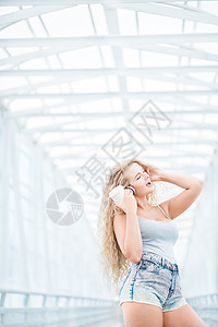 美丽的轻女人戴着音乐耳机,站桥上着咖啡杯,城市背景下摆姿势图片