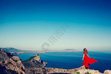 穿着红色连衣裙的轻美女望着山海蓝天背景上的自然女孩时尚照片图片