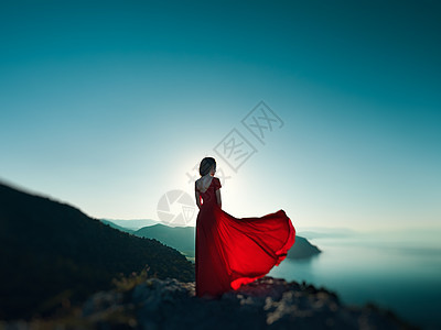 穿着红色连衣裙的轻美女望着山海蓝天背景上的自然女孩时尚照片图片