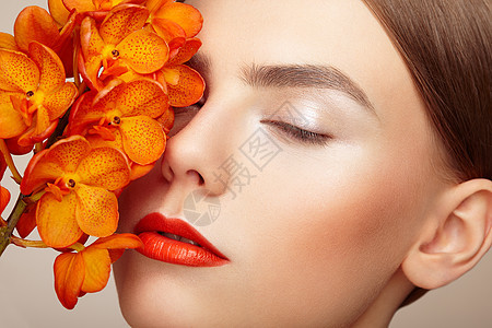 美丽的轻女子兰花的肖像黑发女人,化妆豪华完美的皮肤睫毛化妆品眼影橙色的花图片