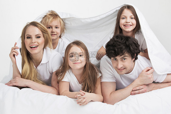 床上微笑的家人带着三个孩子的微笑的家庭床上醒来图片