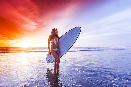冲浪板的女人位美丽的轻苗条的运动女穿着比基尼,穿着冲浪板,日落时站海边图片