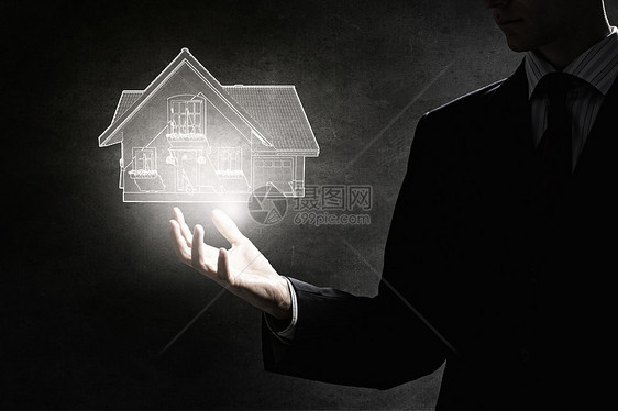 投资建设商人的手着发光的房子模型黑暗的背景图片