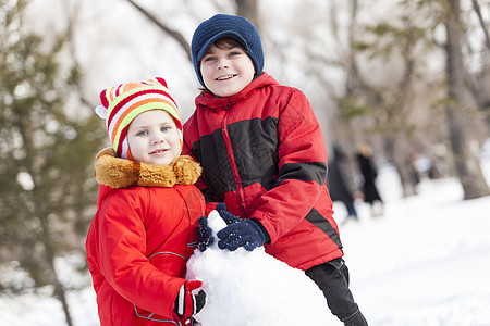 可爱的男孩女孩冬季公园堆雪人冬季活动游戏图片