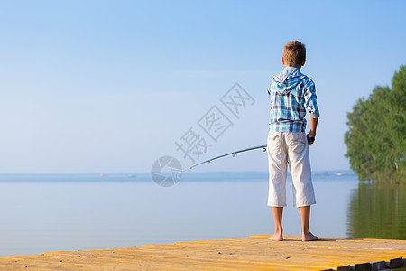穿着蓝色衬衫的男孩站码头上,海边着鱼竿图片
