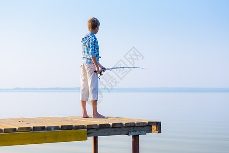 穿着蓝色衬衫的男孩站码头上,海边着鱼竿图片