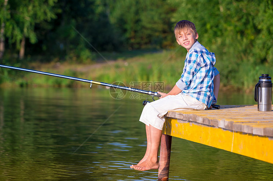 穿着蓝色衬衫的男孩坐海边的码头上,着鱼竿图片