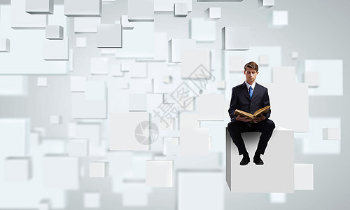英俊的商人坐白色的立方体上看书图片