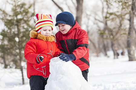 可爱的男孩女孩冬季公园堆雪人冬季活动游戏图片