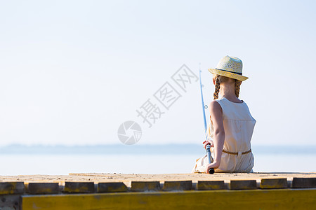 穿着连衣裙帽子的女孩带着钓鱼竿码头钓鱼图片