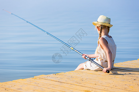 穿着连衣裙帽子的女孩带着钓鱼竿码头钓鱼图片