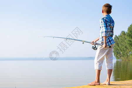 穿着蓝色衬衫的男孩站馅饼上穿着蓝色衬衫的男孩站海边的码头上,着鱼竿图片