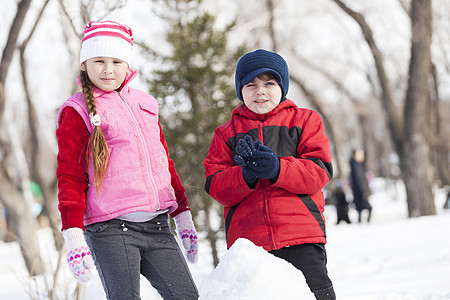 可爱的男孩女孩冬季公园堆雪人冬季活动游戏图片