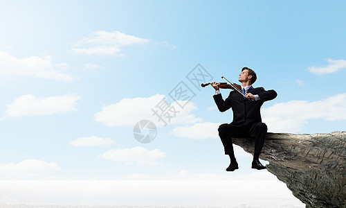 才华的人要站顶端商人坐岩石边缘拉小提琴图片