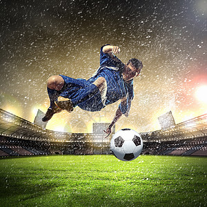 足球运动员击球穿着蓝色衬衫的足球运动员雨下体育场把球打得高高的图片