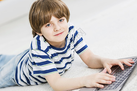游戏笔记本可爱的男孩躺地板上用笔记本电脑玩电脑游戏背景