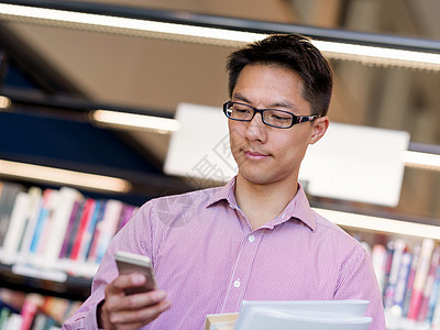 快乐的男学生图书馆书快乐的亚洲男学生图书馆着书他的手机图片