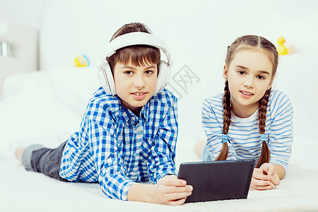 可爱的孩子平板电脑上玩游戏男孩女孩躺地板上用平板电脑背景图片