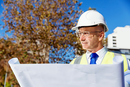 建筑工地的工程师建设者工程师建筑工人施工场景穿着带蓝图的安全背心背景图片
