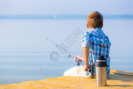 穿蓝色衬衫的男孩坐馅饼上穿着蓝色衬衫的男孩坐海边的码头上,着鱼竿图片