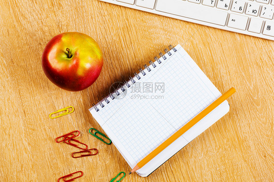 工作场所木制桌子上的红色苹果记事本键盘图片