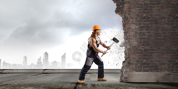 建筑工人强壮的人统的破碎砖墙与图片