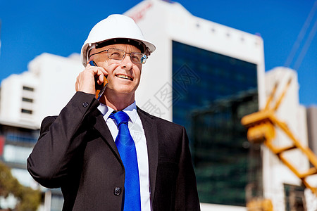 建筑工地的商人施工场景,司机戴着安全帽,带着手机背景图片
