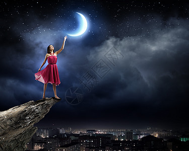 月亮下女孩穿着红色连衣裙的年轻女人站岩石的边缘背景
