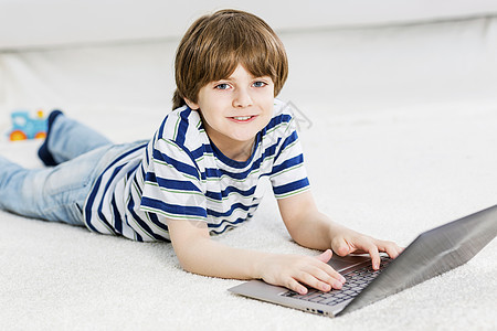 可爱的男孩躺地板上用笔记本电脑玩电脑游戏图片