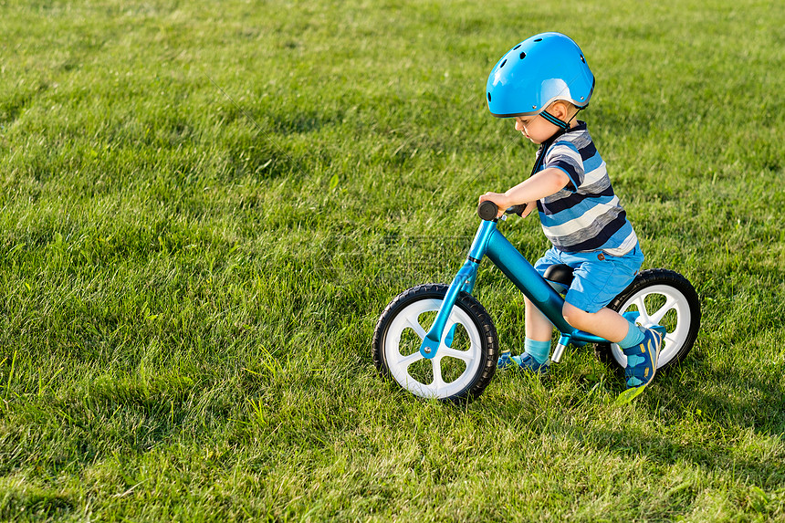 ‘~戴头盔的男孩骑蓝色平衡自行车跑步自行车快乐的孩子学花园里的训练自行车上保持平衡健康的学龄前儿童暑期活动孩子  ~’ 的图片