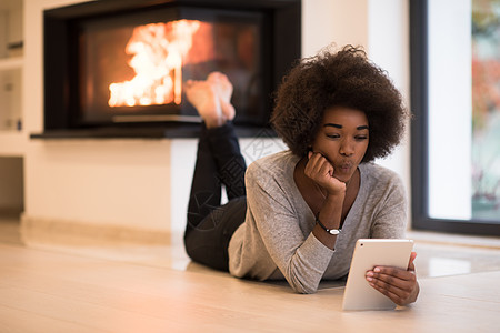 秋天,美丽的轻黑人妇女壁炉前的豪华住宅地板上用平板电脑图片