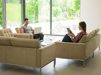 轻夫妇豪华的家里放松,平板电脑笔记本电脑客厅沙发上阅读图片