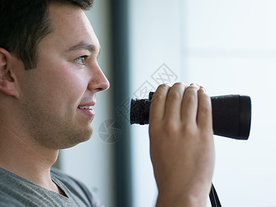 轻人站着,用望远镜透过璃窗看着远处的东西背景图片