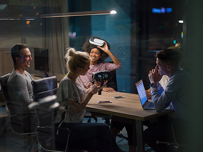 多民族业务队夜间办公会议上用虚拟现实耳机,开发人员创意办公室与虚拟现实模拟器桌子周围开会图片