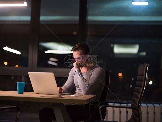 轻人晚上黑暗的办公室里用笔记本电脑工作师稍后的时间工作图片